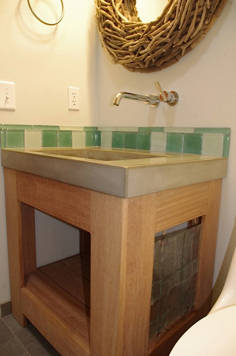 Cette image montre une petite salle d'eau urbaine en bois brun avec un placard en trompe-l'oeil, un plan de toilette en béton, un combiné douche/baignoire, WC à poser, un carrelage vert, un carrelage en pâte de verre et un mur beige.