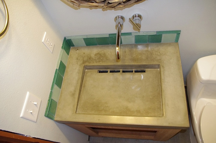 Immagine di una piccola stanza da bagno con doccia industriale con consolle stile comò, ante in legno scuro, top in cemento, vasca/doccia, WC monopezzo, piastrelle verdi, piastrelle di vetro e pareti beige