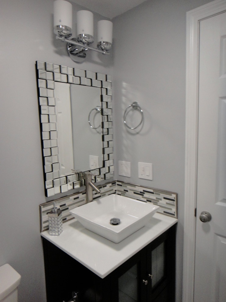 Inredning av ett modernt litet en-suite badrum, med ett fristående handfat, luckor med glaspanel, skåp i mörkt trä, bänkskiva i akrylsten, ett platsbyggt badkar, en dusch/badkar-kombination, en toalettstol med separat cisternkåpa, vit kakel, porslinskakel, grå väggar och klinkergolv i porslin