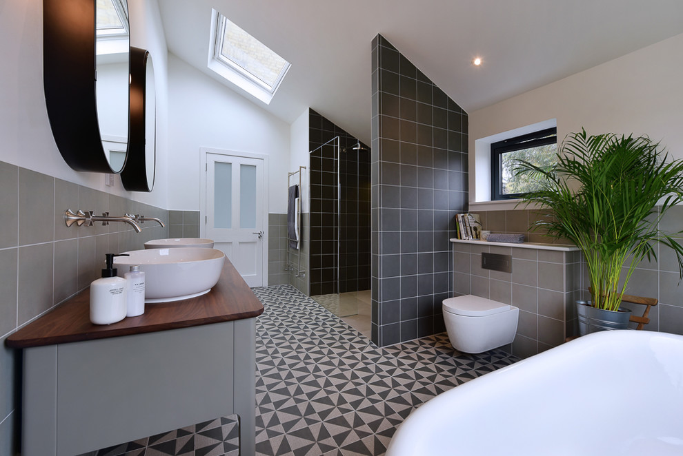 Идея дизайна: главная ванная комната в современном стиле с серыми фасадами, отдельно стоящей ванной, душем в нише, инсталляцией, черной плиткой, серой плиткой, белыми стенами, настольной раковиной, столешницей из дерева, разноцветным полом, открытым душем и коричневой столешницей