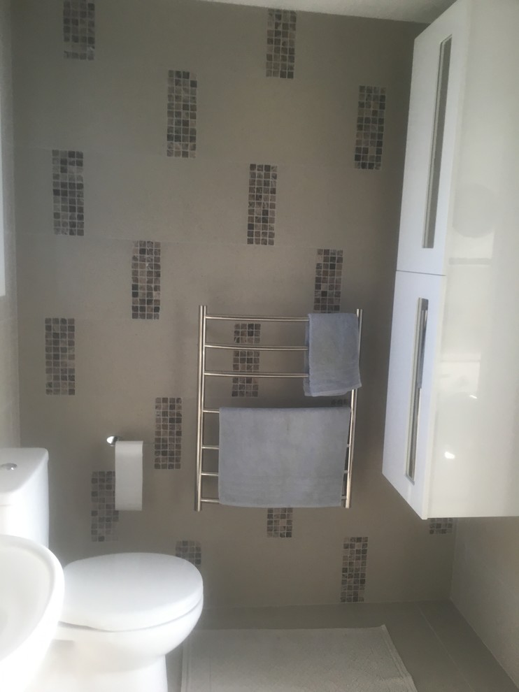 Photo of a medium sized modern ensuite bathroom in Auckland with freestanding cabinets, white cabinets, a built-in bath, a shower/bath combination, a two-piece toilet, multi-coloured tiles, ceramic tiles, multi-coloured walls, ceramic flooring, a pedestal sink and grey floors.
