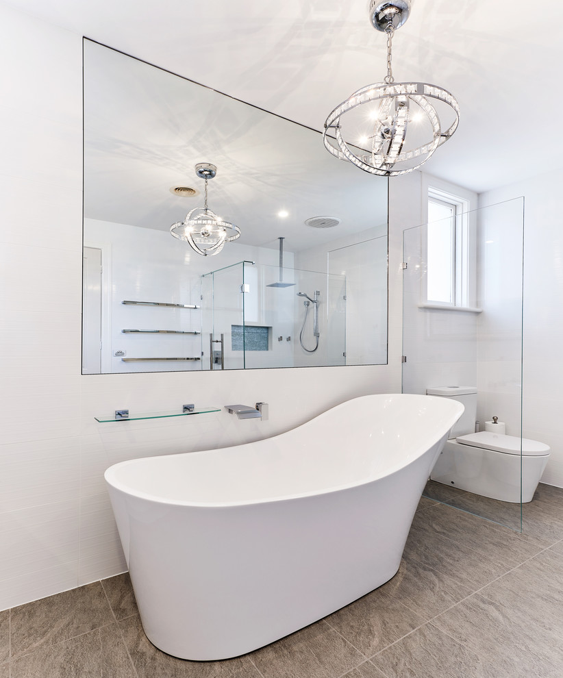 На фото: большая ванная комната в стиле модернизм с отдельно стоящей ванной, угловым душем, раздельным унитазом, белой плиткой, цементной плиткой, белыми стенами, полом из травертина, серым полом и душем с распашными дверями