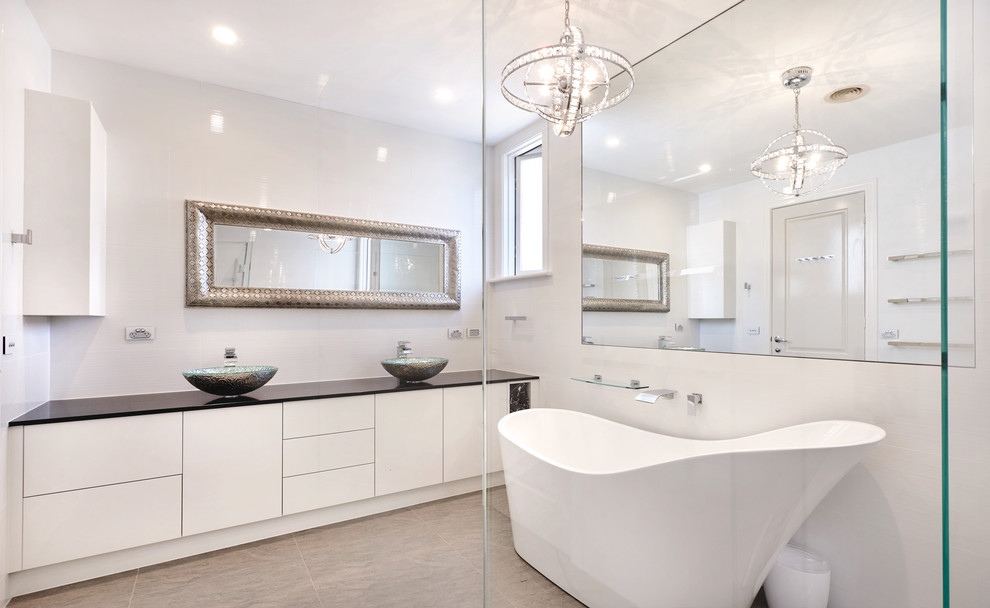 Идея дизайна: большая главная ванная комната в стиле модернизм с отдельно стоящей ванной, угловым душем, раздельным унитазом, белой плиткой, цементной плиткой, белыми стенами, полом из травертина, серым полом и душем с распашными дверями