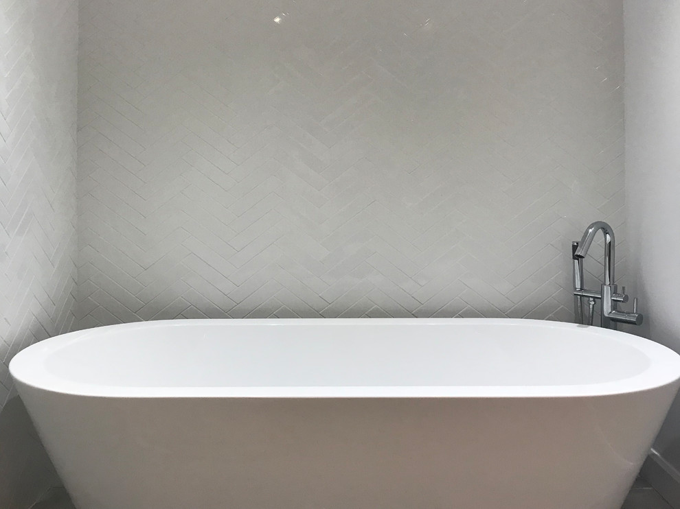 Cette image montre une salle d'eau minimaliste de taille moyenne avec une baignoire indépendante, un carrelage blanc, des carreaux de céramique, un mur blanc, carreaux de ciment au sol et un sol gris.