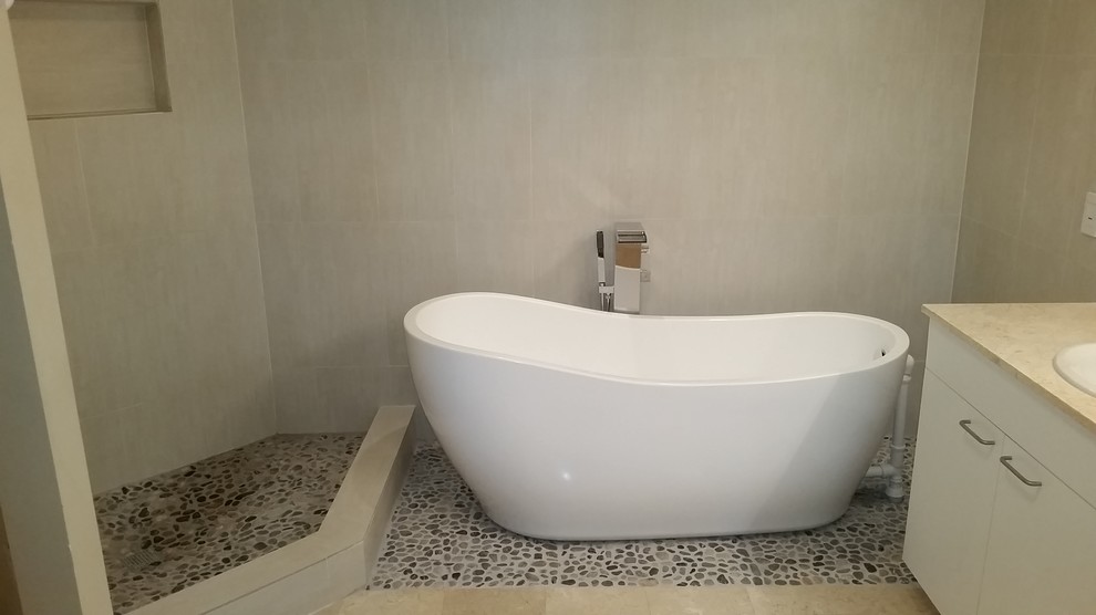 Стильный дизайн: ванная комната в современном стиле с плоскими фасадами, белыми фасадами, отдельно стоящей ванной, бежевой плиткой, керамогранитной плиткой, бежевыми стенами, полом из галечной плитки и накладной раковиной - последний тренд