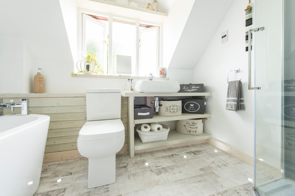 This is an example of a small contemporary family bathroom in Dorset with a freestanding bath, a corner shower, grey walls, laminate floors, grey floors, a hinged door, a one-piece toilet and a vessel sink.