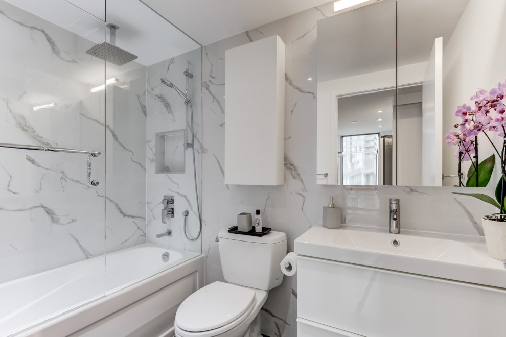 This is an example of a small contemporary ensuite bathroom in Toronto with flat-panel cabinets, white cabinets, an alcove bath, a one-piece toilet, white tiles, porcelain tiles, white walls, porcelain flooring, an integrated sink, grey floors, a hinged door and white worktops.