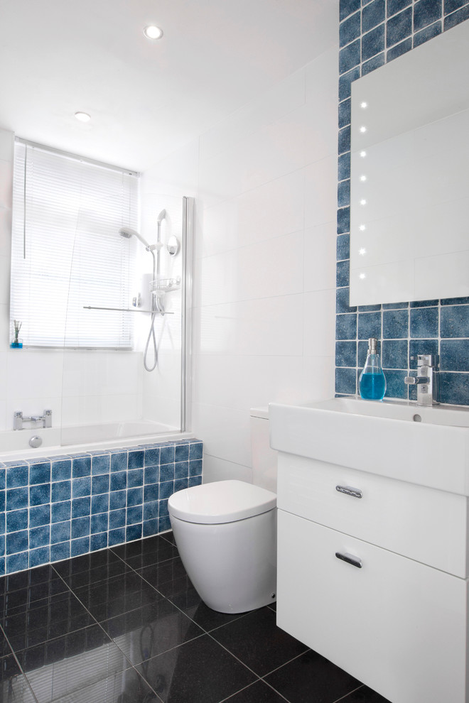 Photo of a medium sized traditional bathroom in Dublin with flat-panel cabinets, white cabinets, blue tiles, a shower/bath combination and black floors.