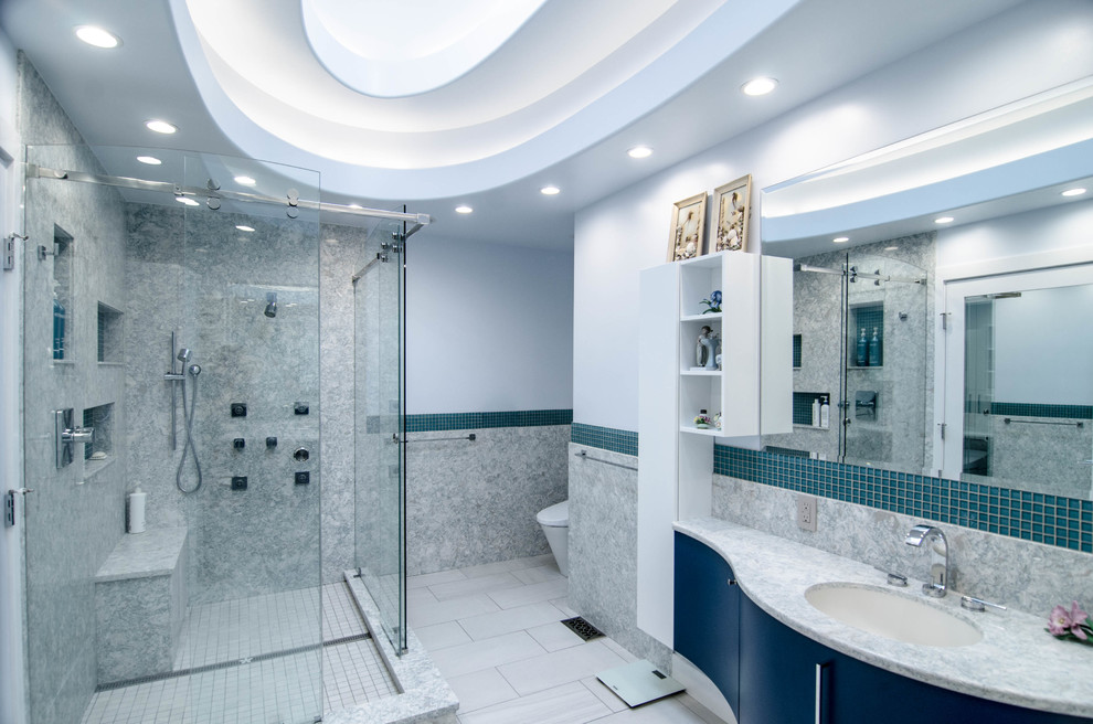 Imagen de cuarto de baño contemporáneo con armarios con paneles lisos, puertas de armario azules, ducha esquinera, baldosas y/o azulejos azules, baldosas y/o azulejos grises, paredes azules, aseo y ducha, lavabo bajoencimera, suelo gris y ducha con puerta corredera