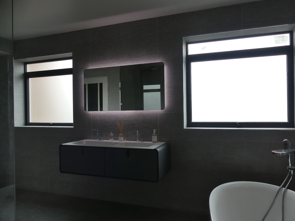 На фото: большая главная ванная комната в стиле модернизм с отдельно стоящей ванной, открытым душем, серой плиткой, керамогранитной плиткой, серыми стенами, полом из керамогранита, подвесной раковиной, серым полом и открытым душем