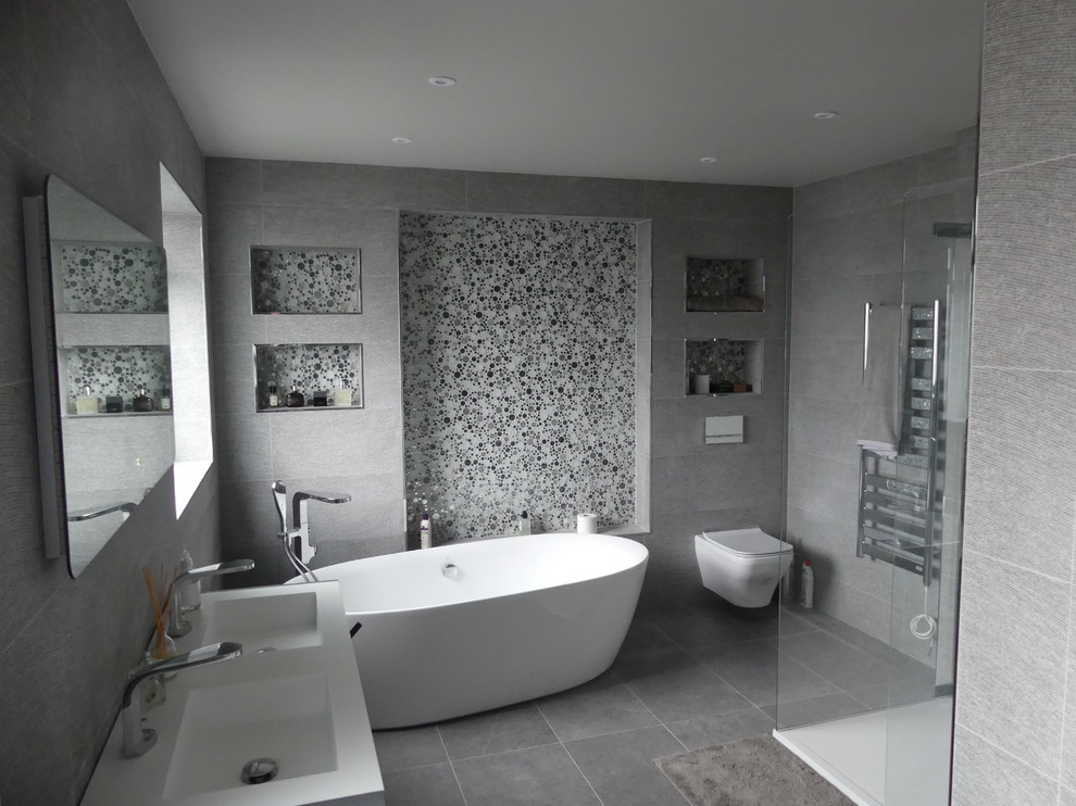 Large modern ensuite bathroom in Hertfordshire with a freestanding bath, a walk-in shower, a wall mounted toilet, grey tiles, porcelain tiles, grey walls, porcelain flooring, a wall-mounted sink, grey floors and an open shower.