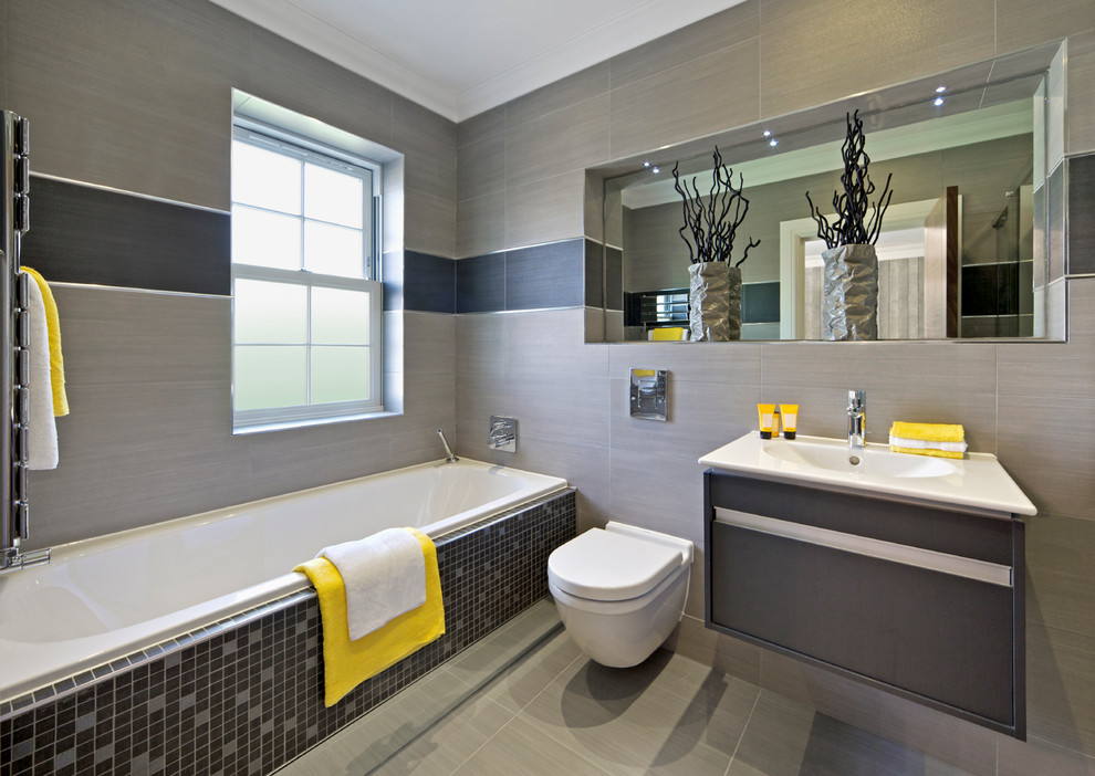 Cette image montre une salle de bain design avec un lavabo intégré, un placard à porte plane, une baignoire posée, WC suspendus, un carrelage gris et un mur gris.