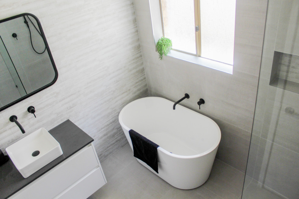 This is an example of a medium sized modern ensuite wet room bathroom in Perth with flat-panel cabinets, white cabinets, a freestanding bath, a two-piece toilet, grey tiles, porcelain tiles, grey walls, porcelain flooring, a vessel sink, engineered stone worktops, grey floors, an open shower and grey worktops.