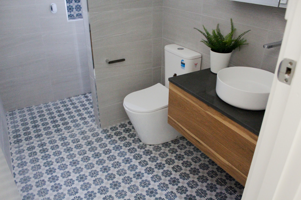Small minimalist 3/4 gray tile and porcelain tile ceramic tile and multicolored floor bathroom photo in Perth with flat-panel cabinets, dark wood cabinets, a one-piece toilet, gray walls, a vessel sink, quartz countertops and black countertops