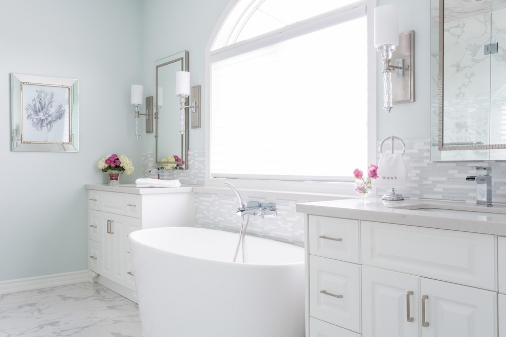 На фото: большая главная ванная комната в классическом стиле с фасадами с выступающей филенкой, отдельно стоящей ванной, врезной раковиной, синими стенами, мраморным полом, белой плиткой, белыми фасадами, удлиненной плиткой, раздельным унитазом и столешницей из гранита