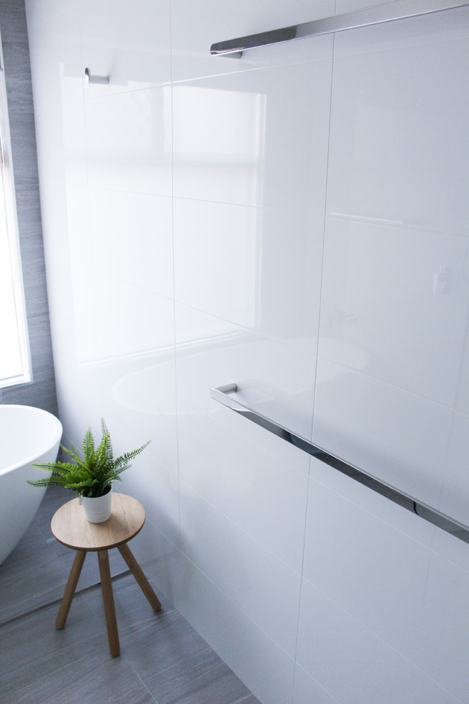 Пример оригинального дизайна: детская ванная комната среднего размера в стиле модернизм с плоскими фасадами, белыми фасадами, отдельно стоящей ванной, открытым душем, унитазом-моноблоком, белой плиткой, керамической плиткой, белыми стенами, полом из керамогранита, настольной раковиной, столешницей из искусственного кварца, серым полом, открытым душем и серой столешницей