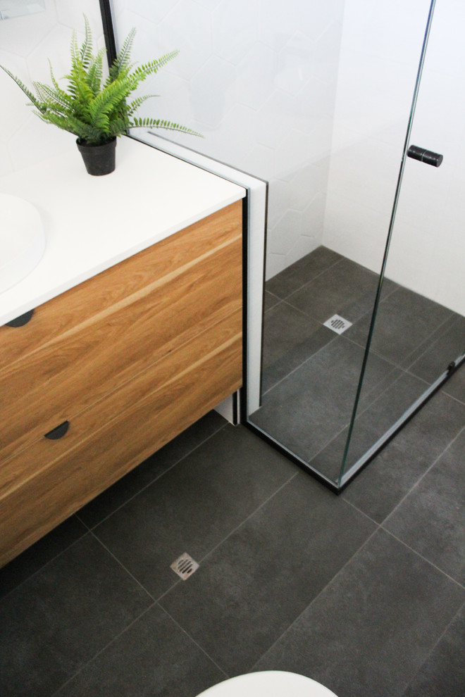 Mid-sized minimalist master white tile and ceramic tile porcelain tile and gray floor corner shower photo in Perth with flat-panel cabinets, dark wood cabinets, a one-piece toilet, white walls, a vessel sink, quartz countertops, a hinged shower door and white countertops