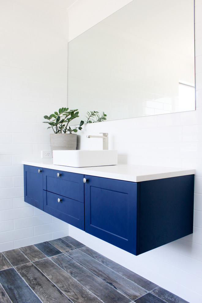 Стильный дизайн: большая главная ванная комната в стиле модернизм с плоскими фасадами, синими фасадами, отдельно стоящей ванной, душем без бортиков, белой плиткой, керамической плиткой, разноцветными стенами, полом из плитки под дерево, настольной раковиной, столешницей из искусственного кварца, разноцветным полом, душем с распашными дверями и белой столешницей - последний тренд