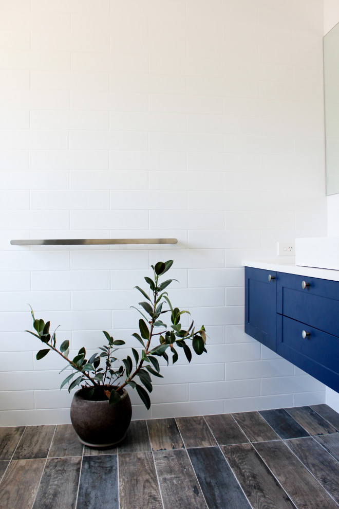 Источник вдохновения для домашнего уюта: большая главная ванная комната в стиле модернизм с фасадами в стиле шейкер, синими фасадами, отдельно стоящей ванной, душем без бортиков, белой плиткой, керамической плиткой, разноцветными стенами, полом из плитки под дерево, настольной раковиной, столешницей из искусственного кварца, разноцветным полом, душем с распашными дверями и белой столешницей