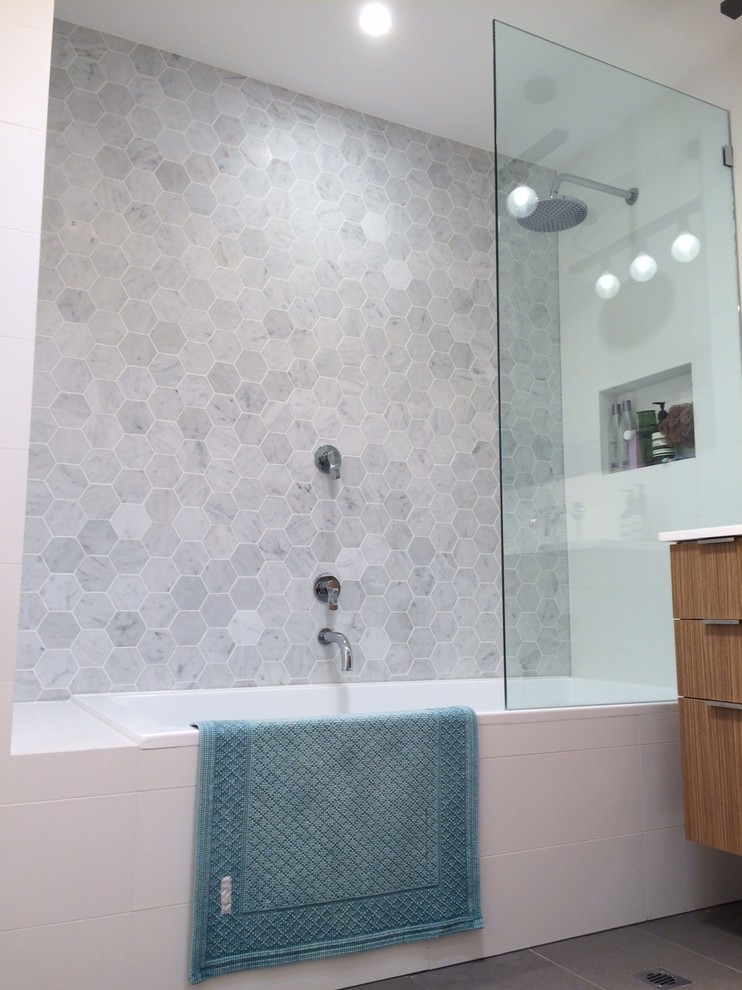 Inredning av ett modernt en-suite badrum, med skåp i mellenmörkt trä, ett platsbyggt badkar, en dusch/badkar-kombination, en vägghängd toalettstol, grå kakel, porslinskakel, vita väggar, klinkergolv i porslin, ett integrerad handfat och bänkskiva i akrylsten