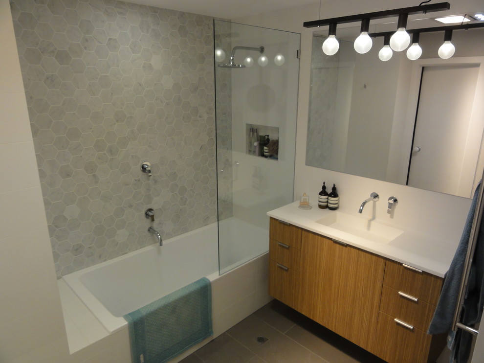 Cette image montre une salle de bain principale design en bois brun avec une baignoire posée, un combiné douche/baignoire, WC suspendus, un carrelage gris, des carreaux de porcelaine, un mur blanc, un sol en carrelage de porcelaine, un lavabo intégré et un plan de toilette en surface solide.