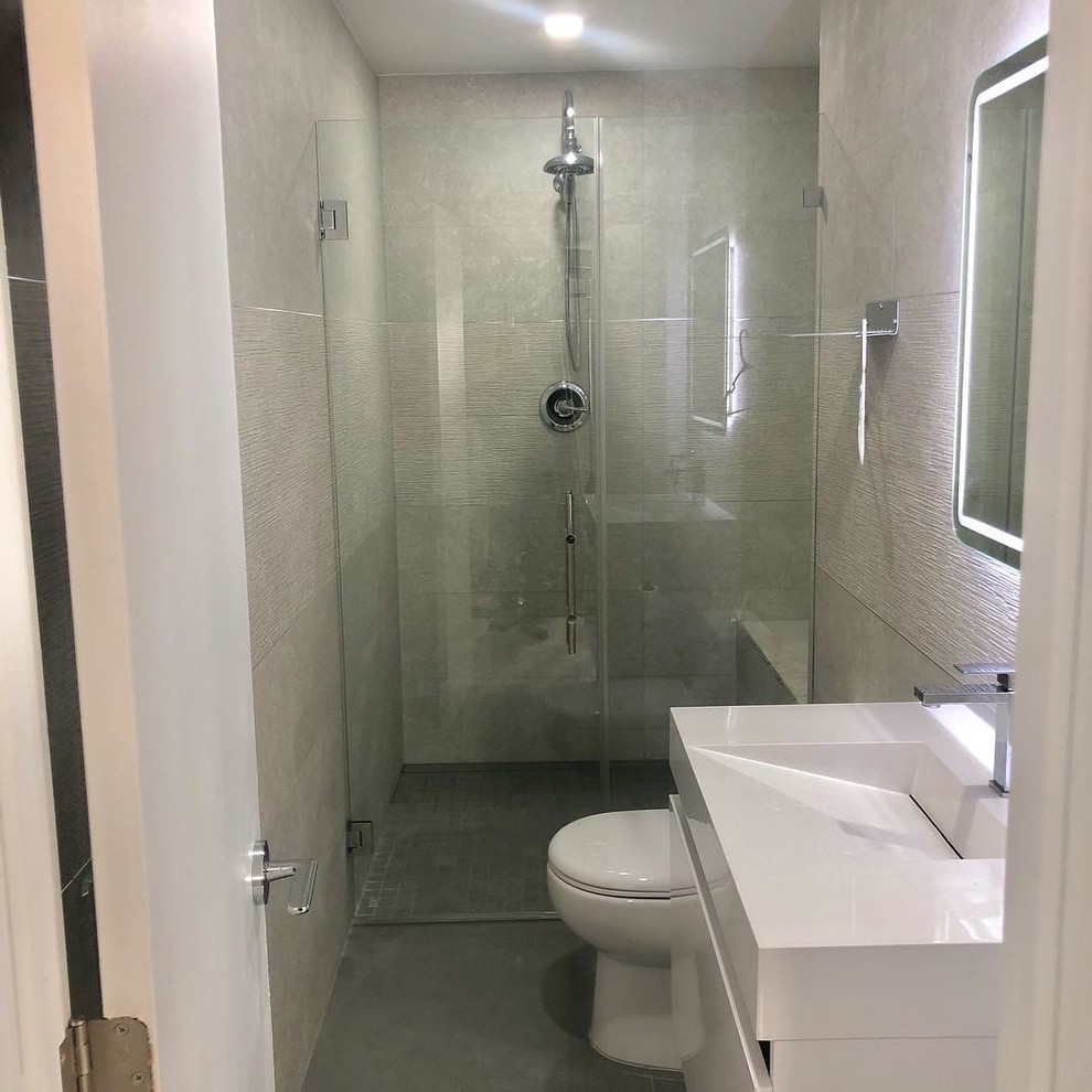 This is an example of a medium sized modern ensuite bathroom in Miami with flat-panel cabinets, white cabinets, a built-in shower, a one-piece toilet, grey tiles, porcelain tiles, grey walls, porcelain flooring, an integrated sink, quartz worktops, grey floors, a hinged door and white worktops.
