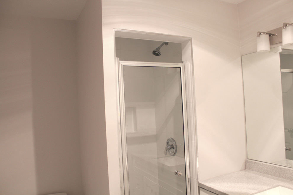 Modern inredning av ett litet en-suite badrum, med ett undermonterad handfat, skåp i shakerstil, vita skåp, bänkskiva i kvarts, en toalettstol med hel cisternkåpa, vit kakel, keramikplattor, vita väggar, klinkergolv i porslin och en dusch i en alkov