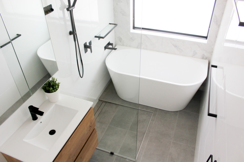 Photo of a medium sized modern ensuite bathroom in Perth with flat-panel cabinets, light wood cabinets, a freestanding bath, a walk-in shower, a one-piece toilet, white tiles, ceramic tiles, white walls, porcelain flooring, an integrated sink, engineered stone worktops, grey floors, an open shower and white worktops.