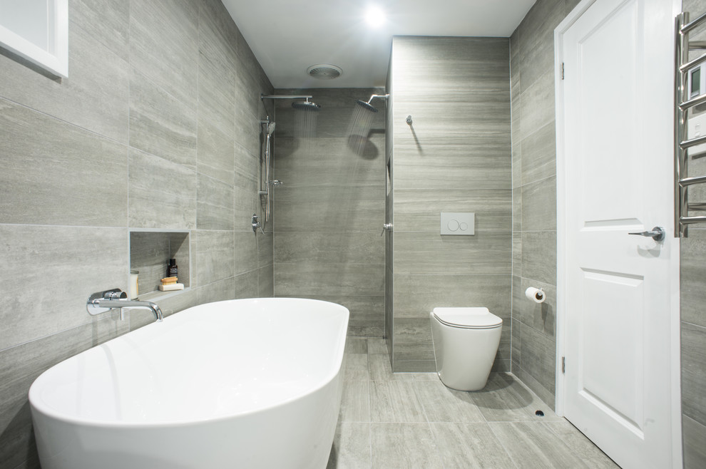 Foto på ett stort funkis en-suite badrum, med ett fristående badkar, en öppen dusch, en toalettstol med hel cisternkåpa, grå kakel, porslinskakel, grå väggar och klinkergolv i porslin