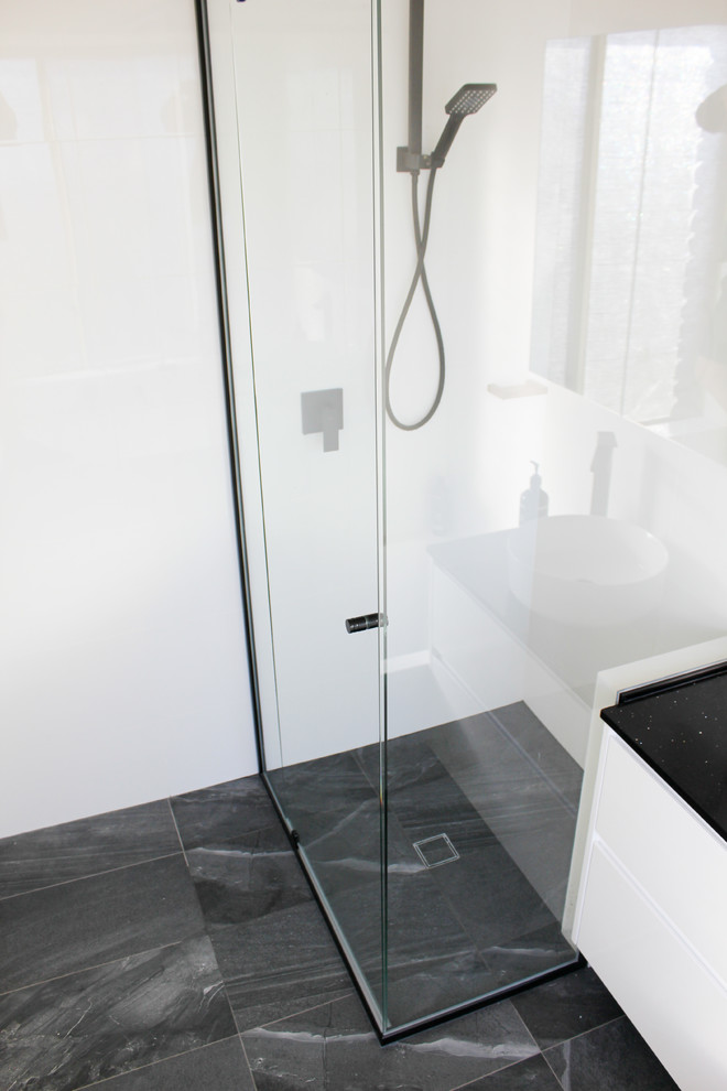 Photo of a small modern family bathroom in Perth with flat-panel cabinets, white cabinets, a built-in bath, a corner shower, white tiles, ceramic tiles, white walls, porcelain flooring, a vessel sink, engineered stone worktops, black floors, a hinged door and black worktops.