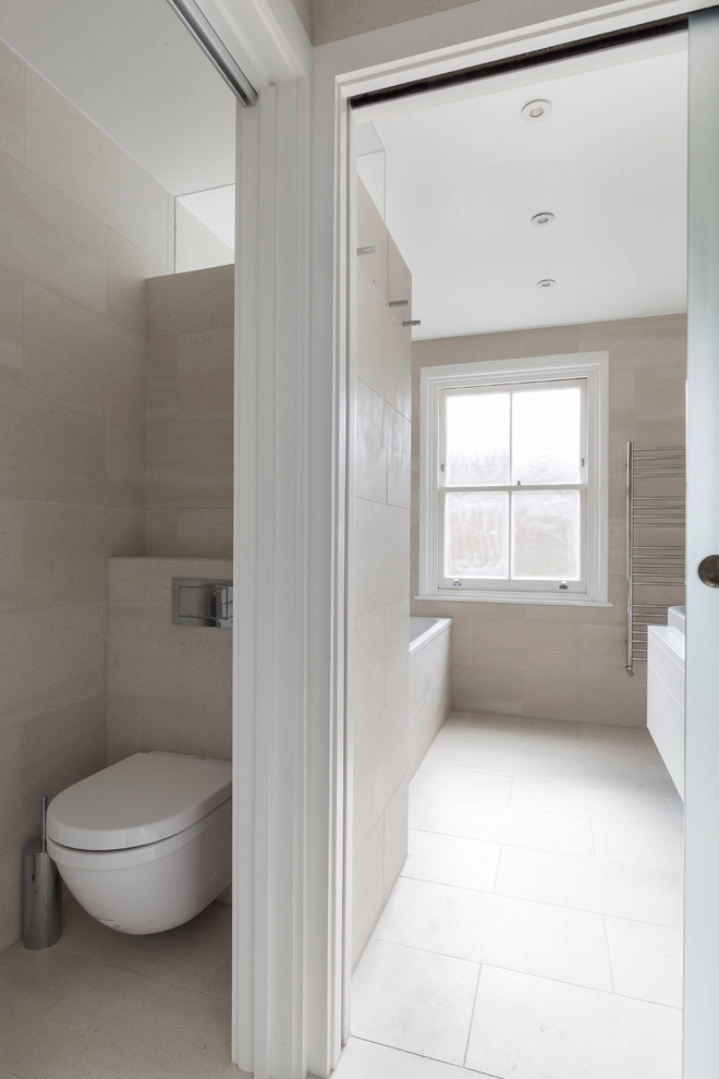 This is an example of a small contemporary family bathroom in London with flat-panel cabinets, white cabinets, a built-in bath, a walk-in shower, a wall mounted toilet, beige tiles, porcelain tiles, beige walls, porcelain flooring, a built-in sink, quartz worktops, beige floors and a sliding door.