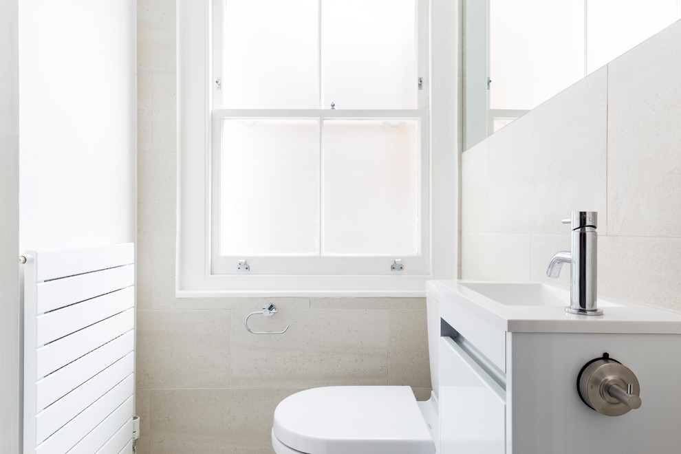 This is an example of a small contemporary family bathroom in London with flat-panel cabinets, white cabinets, a built-in bath, a walk-in shower, a wall mounted toilet, beige tiles, porcelain tiles, beige walls, porcelain flooring, a built-in sink, quartz worktops, beige floors and a sliding door.