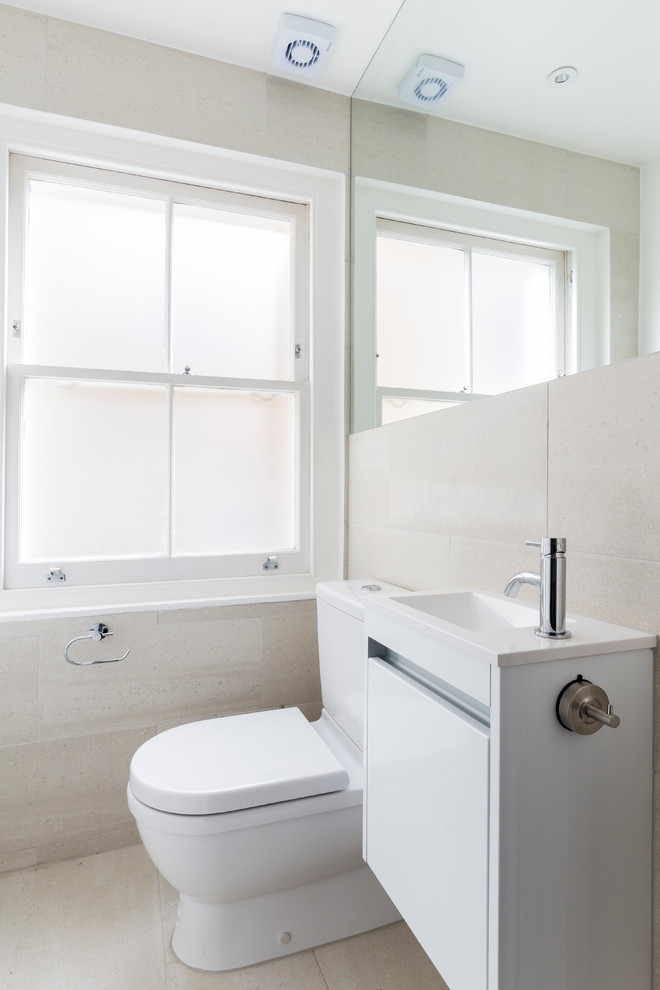 Photo of a small contemporary family bathroom in London with flat-panel cabinets, white cabinets, a built-in bath, a walk-in shower, a wall mounted toilet, beige tiles, porcelain tiles, beige walls, porcelain flooring, a built-in sink, quartz worktops, beige floors and a sliding door.