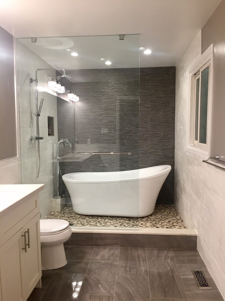 Bild på ett mellanstort vintage badrum med dusch, med svart och vit kakel, grå kakel, klinkergolv i småsten, skåp i shakerstil, vita skåp, ett fristående badkar, en dusch i en alkov, keramikplattor, grå väggar, brunt golv och med dusch som är öppen