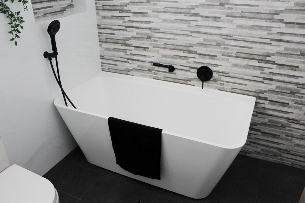 Стильный дизайн: большая главная ванная комната в стиле модернизм с плоскими фасадами, серыми фасадами, отдельно стоящей ванной, угловым душем, унитазом-моноблоком, белой плиткой, каменной плиткой, белыми стенами, полом из керамогранита, монолитной раковиной, столешницей из искусственного камня, черным полом, душем с раздвижными дверями и белой столешницей - последний тренд