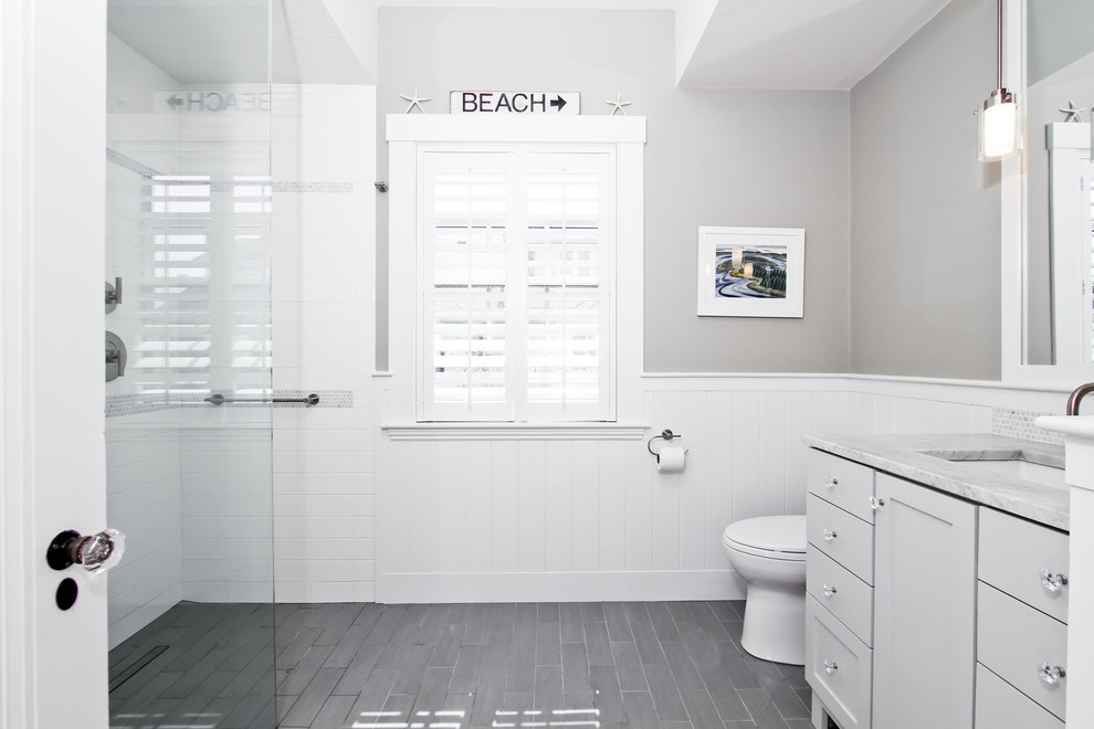 На фото: ванная комната среднего размера в классическом стиле с керамической плиткой, полом из керамической плитки, фасадами с утопленной филенкой, белыми фасадами, душем в нише, унитазом-моноблоком, серой плиткой, серыми стенами, душевой кабиной, врезной раковиной, мраморной столешницей, серым полом и душем с распашными дверями с