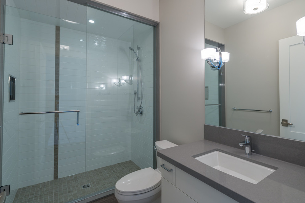This is an example of a small contemporary family bathroom in Toronto with a submerged sink, flat-panel cabinets, white cabinets, solid surface worktops, an alcove shower, a two-piece toilet, white tiles, ceramic tiles, grey walls and porcelain flooring.