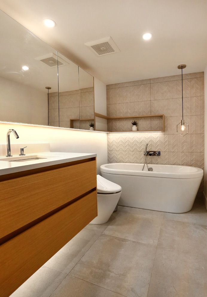 This is an example of a small contemporary ensuite bathroom in Vancouver with flat-panel cabinets, light wood cabinets, a freestanding bath, a one-piece toilet, beige tiles, ceramic tiles, beige walls, concrete flooring, a vessel sink, engineered stone worktops and multi-coloured floors.