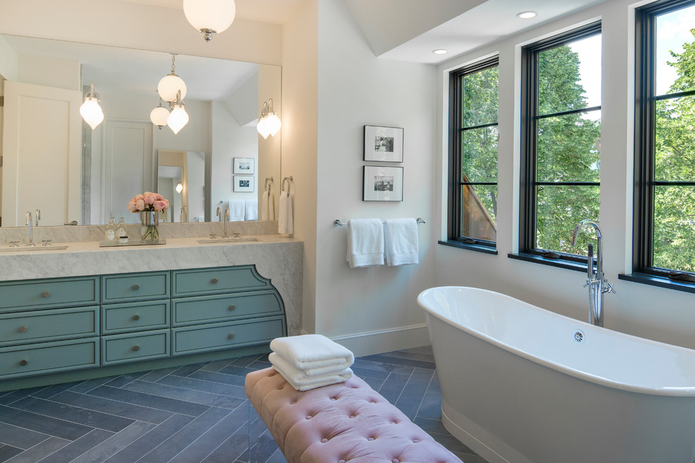 This is an example of a large traditional ensuite bathroom in Minneapolis with a submerged sink, raised-panel cabinets, blue cabinets, marble worktops, a freestanding bath, a corner shower, a one-piece toilet, white tiles, metro tiles, white walls and porcelain flooring.