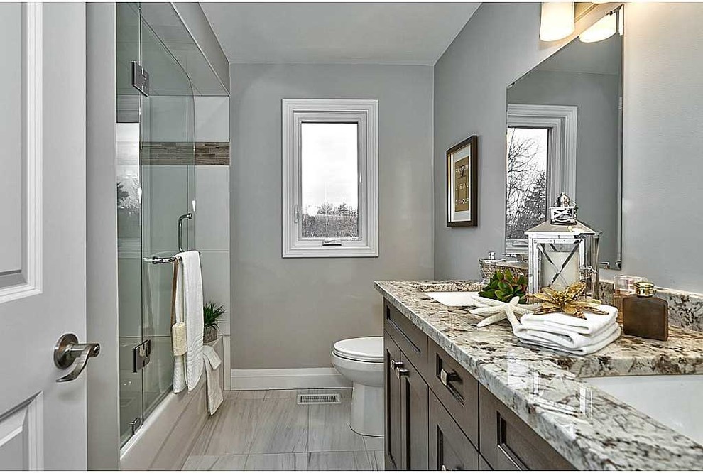 Mid-sized transitional 3/4 porcelain tile and gray floor alcove shower photo in Toronto with recessed-panel cabinets, dark wood cabinets, a two-piece toilet, gray walls, an undermount sink, granite countertops and a hinged shower door