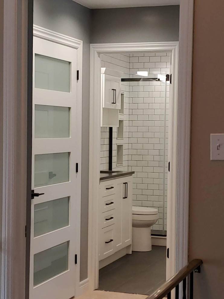 Photo of a medium sized classic ensuite bathroom in Other with shaker cabinets, white cabinets, an alcove shower, a one-piece toilet, white tiles, metro tiles, porcelain flooring, a submerged sink, quartz worktops, grey floors, a sliding door, black worktops, a wall niche, double sinks and a built in vanity unit.