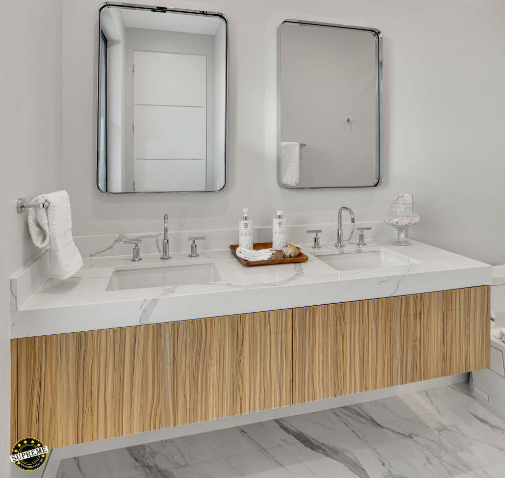 Inspiration for a medium sized modern ensuite bathroom in Los Angeles with flat-panel cabinets, light wood cabinets, an alcove bath, a shower/bath combination, a one-piece toilet, white walls, marble flooring, a submerged sink, marble worktops, white floors, a hinged door, white worktops, a wall niche, double sinks and a built in vanity unit.