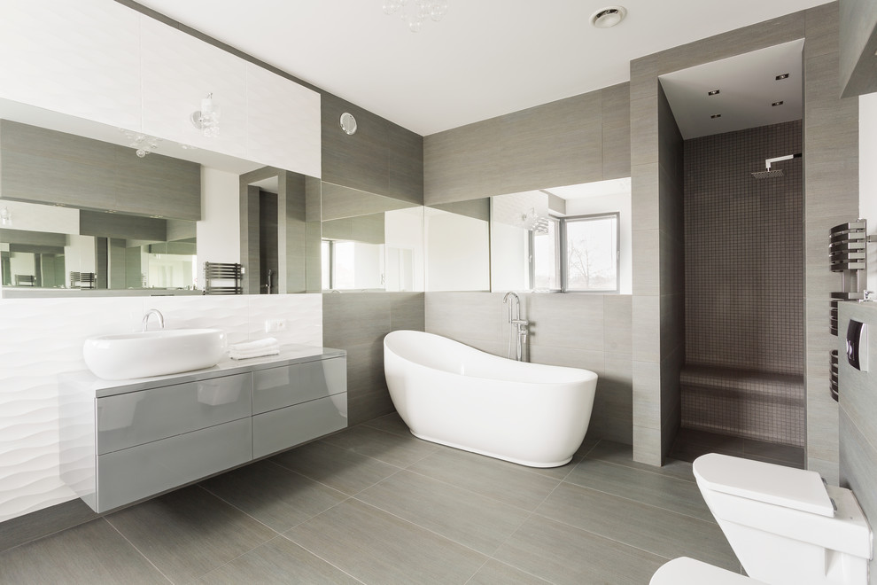 This is an example of a large contemporary ensuite bathroom in Melbourne with a walk-in shower, porcelain tiles, grey walls, porcelain flooring, a vessel sink, solid surface worktops, an open shower, flat-panel cabinets, grey cabinets, a freestanding bath, a bidet, beige tiles and beige floors.