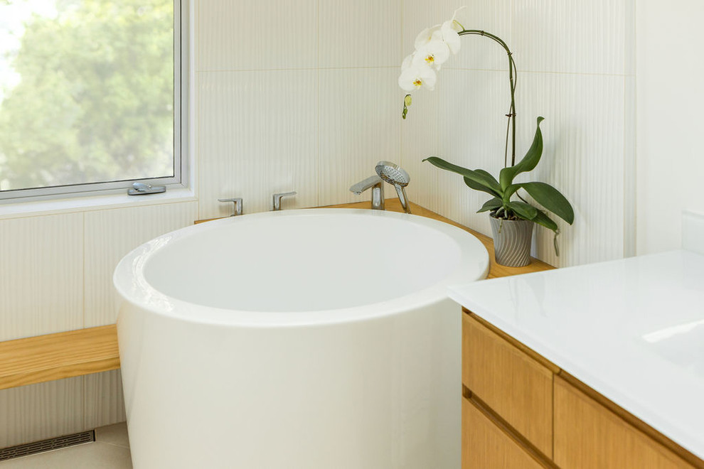 На фото: большая главная ванная комната в современном стиле с плоскими фасадами, светлыми деревянными фасадами, японской ванной, душем без бортиков, унитазом-моноблоком, белой плиткой, керамической плиткой, белыми стенами, полом из керамической плитки, монолитной раковиной, стеклянной столешницей, белым полом, шторкой для ванной и белой столешницей с