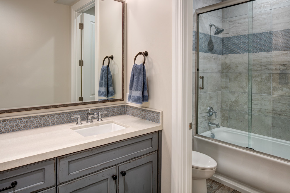 Photo of a large classic family bathroom in Salt Lake City with recessed-panel cabinets, blue cabinets, a built-in bath, a shower/bath combination, a one-piece toilet, grey tiles, ceramic tiles, beige walls, ceramic flooring, a submerged sink, granite worktops, beige floors, a sliding door and white worktops.