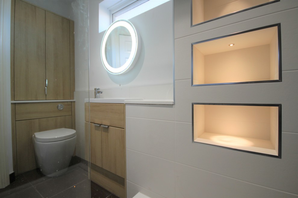 Double shower - contemporary kids' white tile and ceramic tile double shower idea in Cardiff with flat-panel cabinets, light wood cabinets, a wall-mount toilet, white walls, a drop-in sink and solid surface countertops