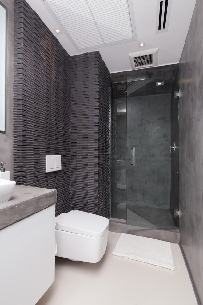 Immagine di una piccola stanza da bagno con doccia contemporanea con ante lisce, ante in legno chiaro, top in cemento, doccia ad angolo, WC sospeso, piastrelle nere e piastrelle di cemento