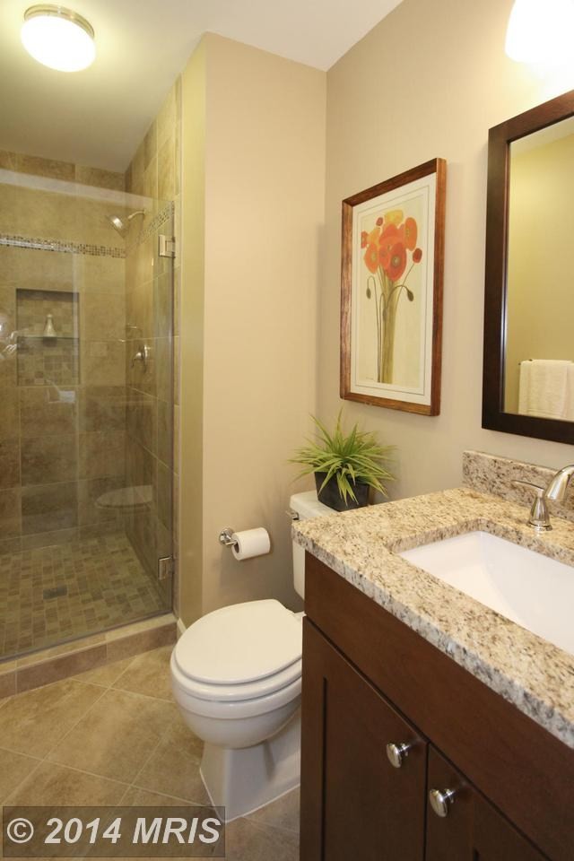 This is an example of a medium sized contemporary shower room bathroom in DC Metro with a submerged sink, recessed-panel cabinets, dark wood cabinets, granite worktops, a built-in bath, a two-piece toilet, beige tiles, porcelain tiles, black walls and porcelain flooring.