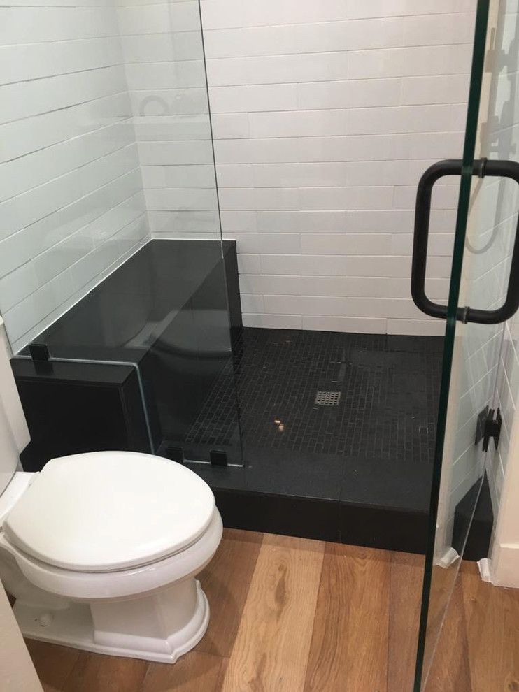 Mid-sized trendy 3/4 medium tone wood floor and brown floor alcove shower photo in Orange County with raised-panel cabinets, black cabinets, a one-piece toilet, white walls, an undermount sink, quartz countertops, a hinged shower door and white countertops