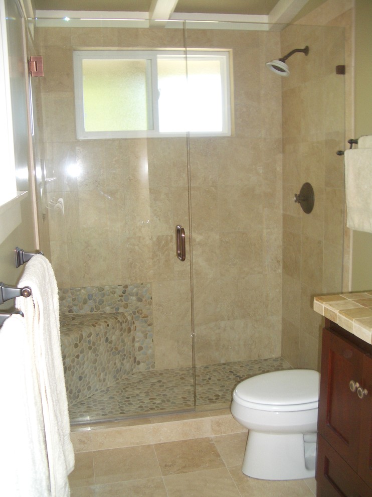 Photo of a small classic shower room bathroom in Orange County with shaker cabinets, dark wood cabinets, an alcove shower, a two-piece toilet, beige tiles, stone tiles, green walls, travertine flooring, a built-in sink and tiled worktops.